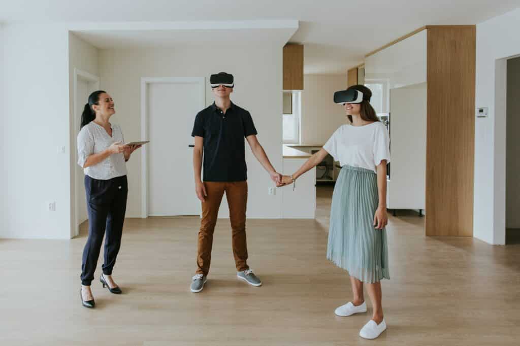 Estate agent with young couple wearing VR headsets in new apartment.